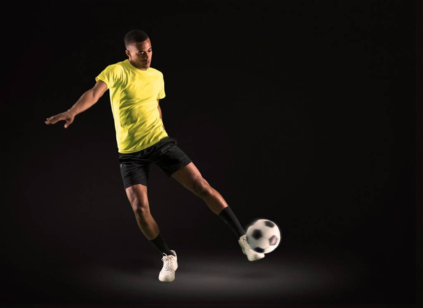 Άνθρωπος παίκτης ποδοσφαίρου με σκοτάδι εκδορά παίζοντας κλωτσάει την μπάλα σε σκούρο φόντο - Φωτογραφία, εικόνα