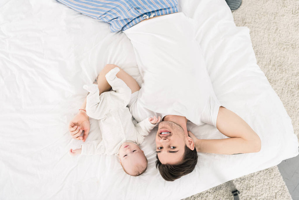 vista aérea del joven padre y el pequeño bebé acostados en la cama juntos en casa
 - Foto, Imagen