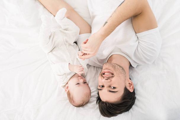 vue aérienne du père souriant et du petit bébé couchés sur le lit ensemble à la maison
 - Photo, image