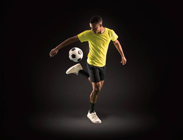 Jogador de futebol homem com pele escura jogando no fundo escuro
 - Foto, Imagem