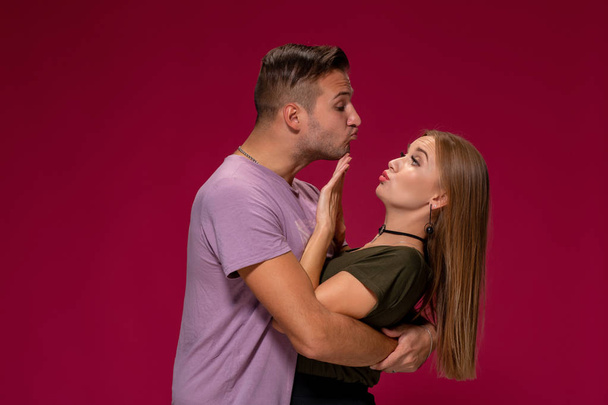 Портрет возмущенной недовольной женщины, жест остановиться рукой, в то время как мужчина пытается поцеловать ее на бордовом фоне
 - Фото, изображение