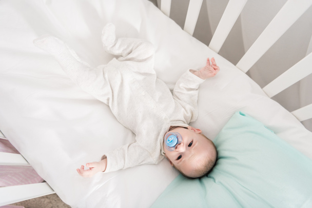 overhead view of little baby with pacifier lying in crib - Φωτογραφία, εικόνα