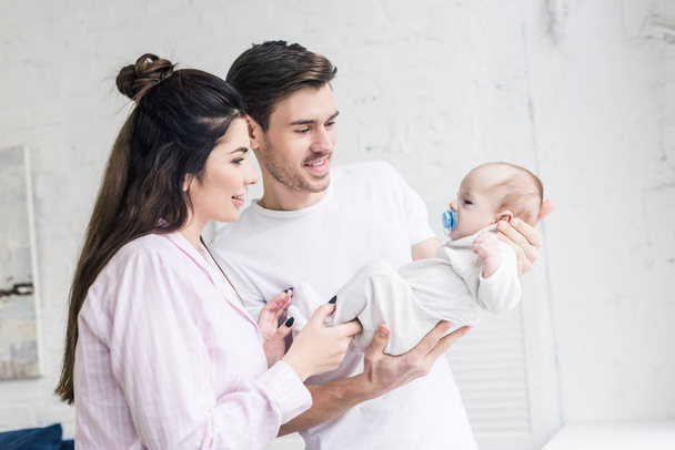 side view of happy parents looking at little son with pacifier at home - Fotoğraf, Görsel