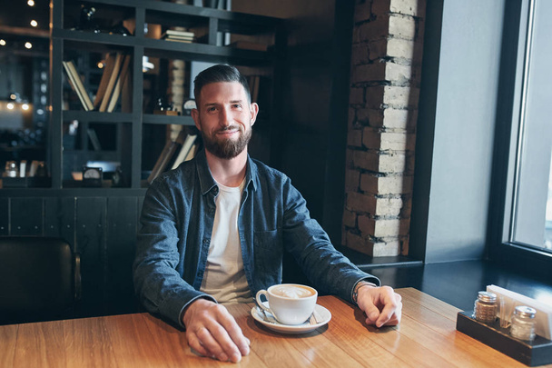 Молодий щасливий бородатий чоловік п'є ранкову свіжу каву
. - Фото, зображення