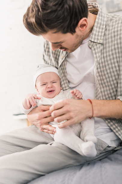 Porträt eines Vaters, der ein weinendes Baby in Händen hält - Foto, Bild