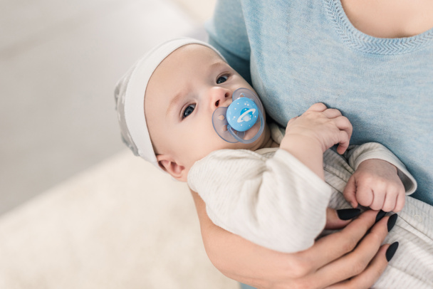 cropped shot of mother holding little son with pacifier in hands - Фото, изображение