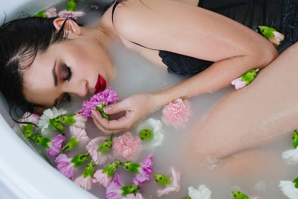 beautiful sexy sad young slim brunette woman in spa - bathroom with water and flowers - Photo, Image