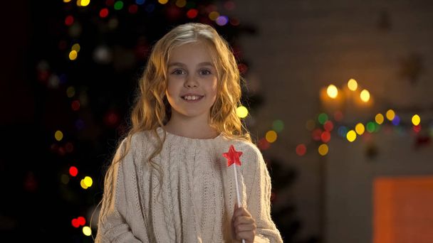 Little girl with magic wand making wishes on Christmas eve, childhood dreams - Фото, изображение