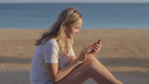 girl with mobile phone at the beach at summer travel at the sea - Кадри, відео
