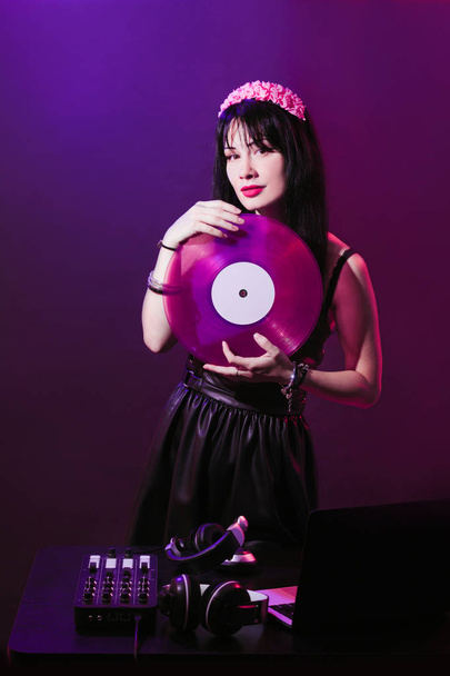 Молода ді-джейка з рожевим вінілом насолоджується музикою. Гламурна дівчина з фоном на фіолетовому фоні грає музику диско
. - Фото, зображення
