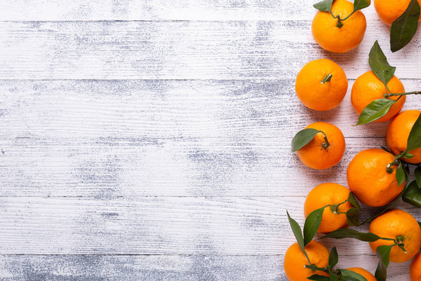 Fresh orange mandarins, tangerine with green leaves on white wooden background. Top view. Copy space - Zdjęcie, obraz