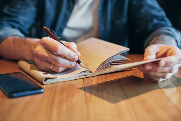 Człowiek ręcznie piórem, pisanie na notebook na drewnianym stole. Szczelnie-do góry - Zdjęcie, obraz