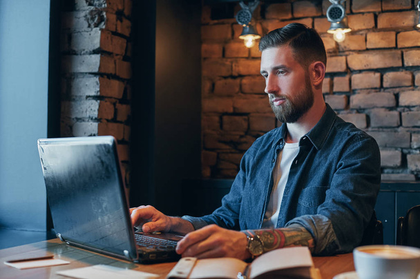 Przystojny młody mężczyzna pracujący na laptopie delektując się kawą w kawiarni - Zdjęcie, obraz