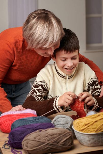 Maman apprend à tricoter son fils. Des fils de laine colorés sont sur la table en bois
. - Photo, image