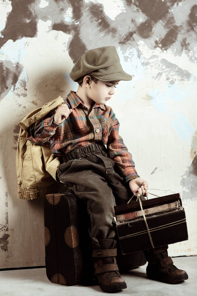 Boy sitting on luggage holding books, retro stylized shot, 50s-60s - Fotoğraf, Görsel