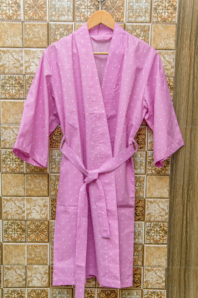 Color cotton bathrobes for the hotel. Pink and white bathrobes with a circle pattern. Light summer dressing gowns with a belt. Bathrobe hanging on a hanger. Home textiles in the interior. - Photo, Image