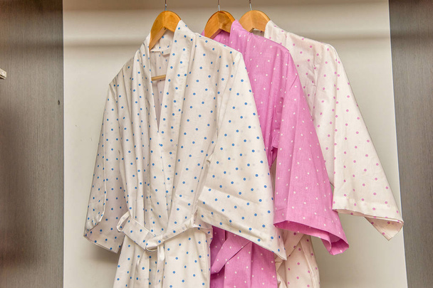 Color cotton bathrobes for the hotel. Pink and white bathrobes with a circle pattern. Light summer dressing gowns with a belt. Bathrobe hanging on a hanger. Home textiles in the interior. - Foto, immagini