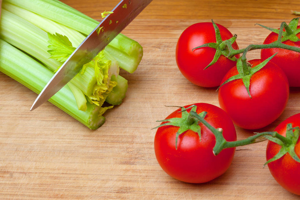 Fusti verdi di sedano e pomodori rossi su un tagliere di legno accanto a un coltello di ferro
 - Foto, immagini