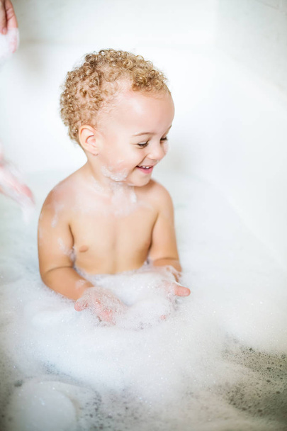 Closeup two year old child having fun with foam by bathing in bathtub. The symbol of purity and hygiene education. - Fotoğraf, Görsel