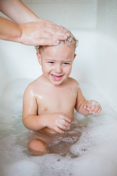 Cute two year old boy taking a relaxing bath with foam - Foto, afbeelding