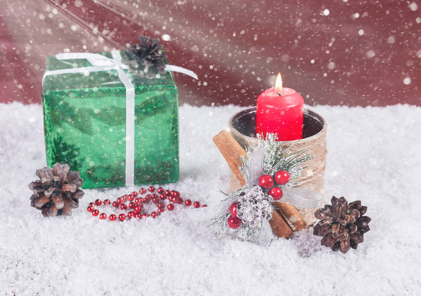 Red candle in a candlestick in the snow with elements of New Year's decor - 写真・画像