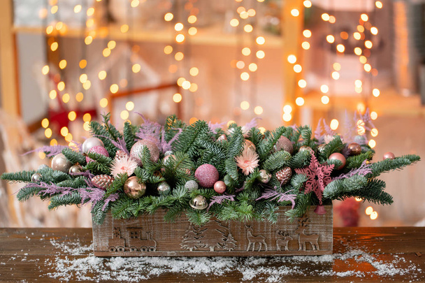 Bel arrangement festif d'épinette fraîche, plantes ornementales roses dans une boîte en bois rustique. L'humeur de Noël. Garland bokeh sur fond
. - Photo, image