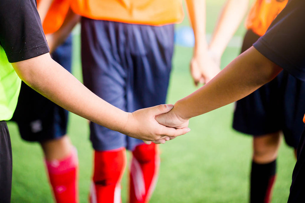 Юные футболисты хлопают руками для тренировок по футболу. Футболисты и вратарь движутся рука об руку
. - Фото, изображение