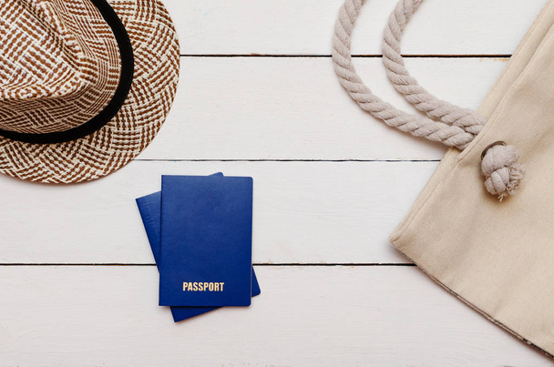 На деревянном столе лежит шляпа, пляжная сумка и два паспорта
 - Фото, изображение