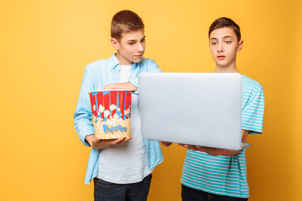 Two teen friends with a bucket of popcorn in their hands and a laptop preparing to watch movies - Foto, Bild