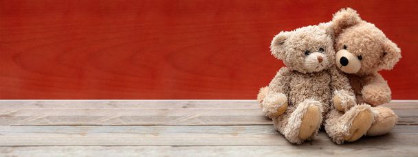Love, friendship concept, tight hug. Two teddy bears embracing as a couple on wooden floor, red wall background, banner, copy space. - Photo, Image