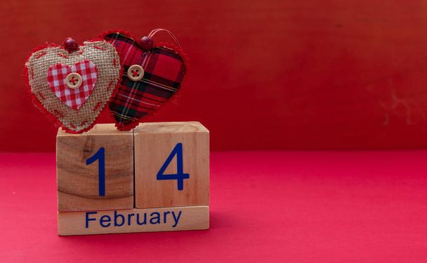 Saint Valentin. Calendrier cubes en bois avec texte 14 Février et deux coeurs en tissu rouge, sur fond rouge, espace de copie
 - Photo, image