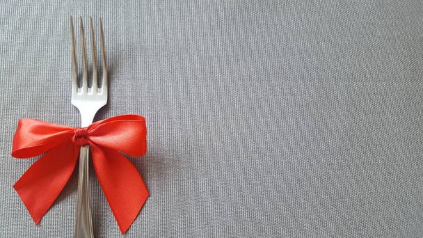 A fork with a red bow lies on the tablecloth. Empty space to insert text. Photo for the menu of cafe, restaurant, dining room, pizzeria. - Photo, Image