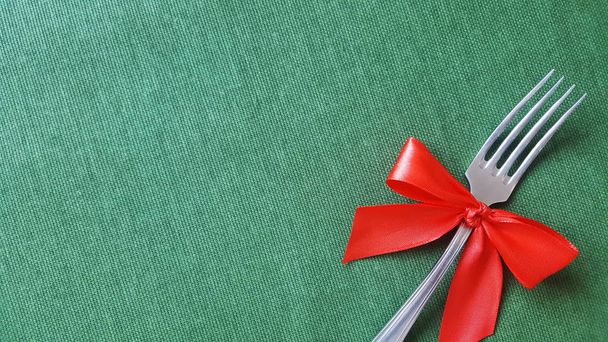 A fork with a red bow lies on the tablecloth. Empty space to insert text. Photo for the menu of cafe, restaurant, dining room, pizzeria. A place for a festive menu. - Foto, afbeelding