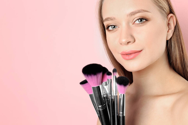 Portrait of beautiful young woman with makeup brushes on color background. Space for text - Foto, Bild