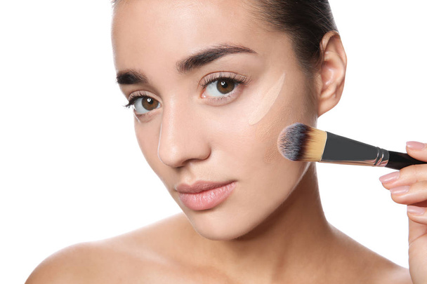 Young woman applying foundation on her face against white background - Photo, image