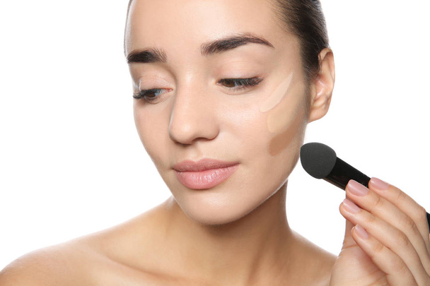 Young woman applying foundation on her face against white background - Foto, Bild