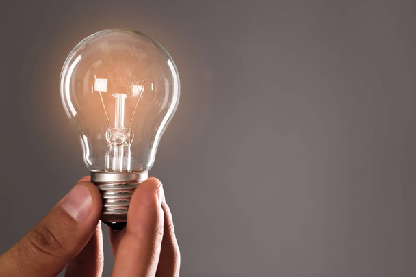 Man holding lamp bulb against gray background, closeup. Space for text - Zdjęcie, obraz