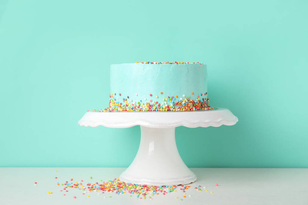 Fresh delicious birthday cake on stand against color background - Foto, afbeelding