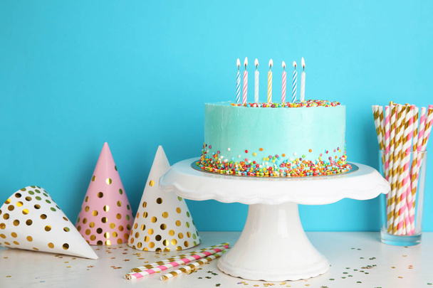 Fresh delicious cake and birthday caps on table against color background. Space for text - Foto, Bild
