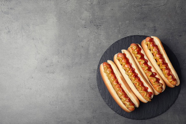Slate plate with hot dogs on grey background, top view. Space for text - Fotoğraf, Görsel