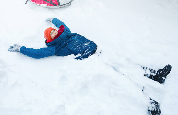 cute young boy in  hat blue jacket holds and plays with snow, has fun, smiles, makes snowman in winter park. Active lifestyle, winter activity, outdoor winter games, snowballs.  - Photo, Image