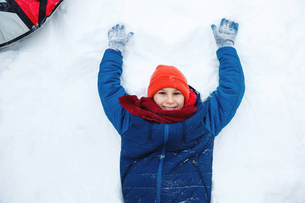 χαριτωμένο νεαρό αγόρι στο καπέλο μπλε σακάκι κατέχει και παίζει με το χιόνι, έχει τη διασκέδαση, χαμόγελα, κάνει χιονάνθρωπος χειμώνα πάρκο. Ενεργό τρόπο ζωής, χειμερινή δραστηριότητα, υπαίθρια χειμερινούς αγώνες, χιονόμπαλες.  - Φωτογραφία, εικόνα