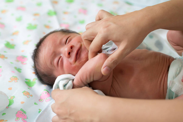 Mutter wechselt Babykleidung, zieht Neugeborenes an - Foto, Bild