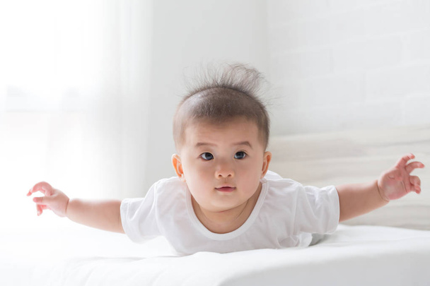 Азиатский мальчик лежит вверх ногами на кровати в белой спальне
 - Фото, изображение