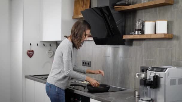 Beautiful brunnete girl cooking dinner in home kitchen, frying on a pan. - Materiał filmowy, wideo