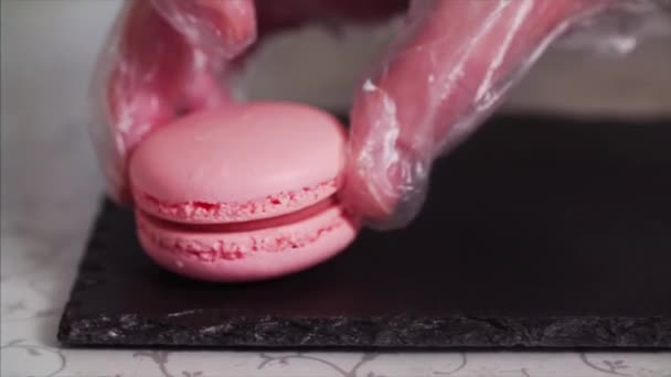 Sliding extreme close up view of pink macaroons or macarons chief putting on black tray - Imágenes, Vídeo