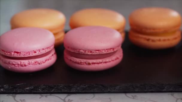 Sliding extreme close up view of orange and pink macaroons or macarons chief putting on black tray - Filmagem, Vídeo