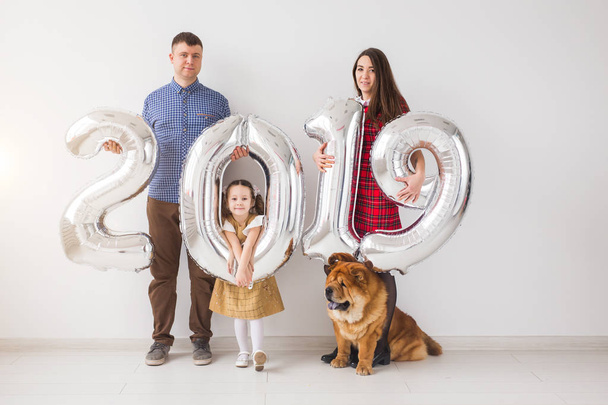 Neues Jahr 2019 naht - gut gelaunte Mutter, Vater, Tochter und Hund halten silberfarbene Nummern in den Händen. - Foto, Bild
