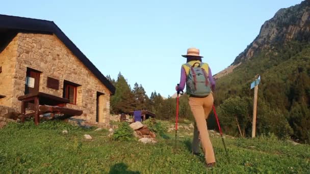 Active hiker woman walks on a path leading to tourist shelter in mountains - Footage, Video