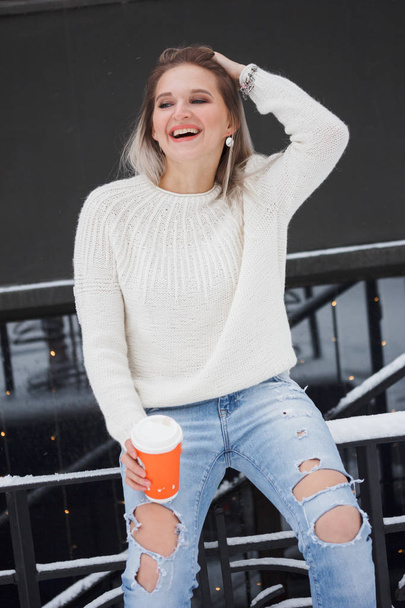 Beautiful natural young smiling shy friendly blonde woman wearing knitted sweater on a grey background. - Photo, image